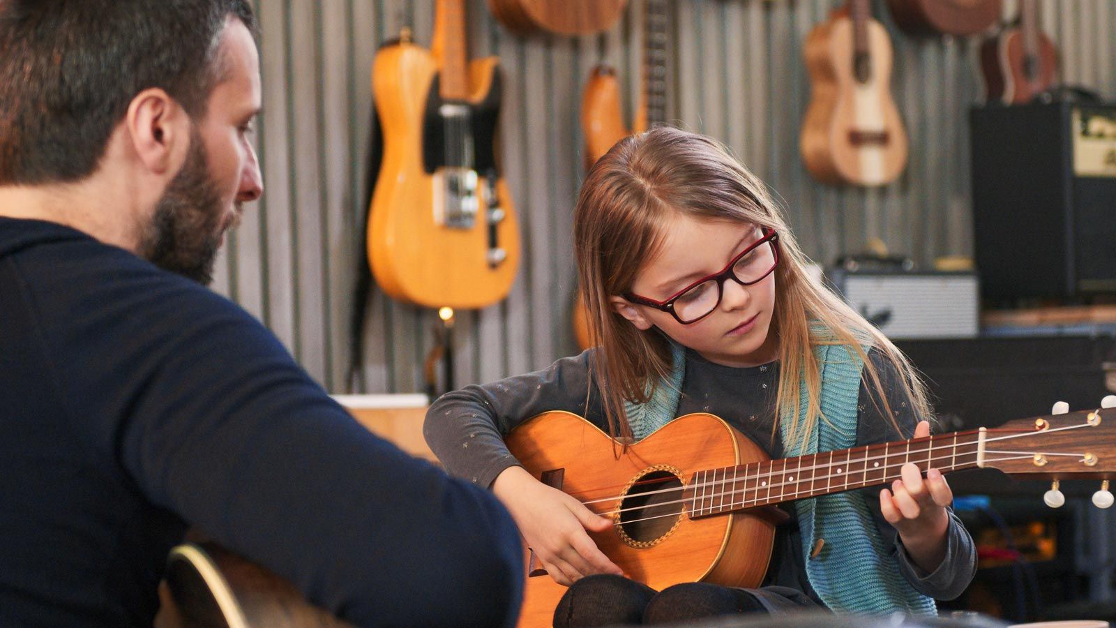 Young girl playing guitar with instructor